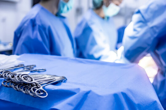 Surgical clamps and medical equipment on surgical tray.Team of doctors or surgeon in blue uniform intends to blur background inside operating room.Copy space on surgical tray with light effect.