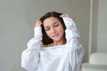 Naklejka premium Happy young woman feeling relaxed with eyes closed. Young brunette woman in white shirt. Minimalistic portrait