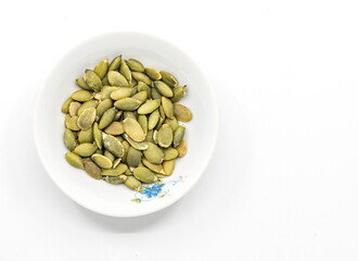 Isolated pumpkin seeds in a small white plate on white background, close-up pumpkin seeds, top view image.