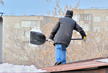 A woman shovels snow off the roof on a spring day