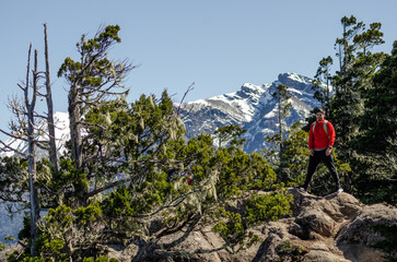 hombre en la cima de un cerro, sobre una roca, observando el paisaje de lagos y montañas nevadas