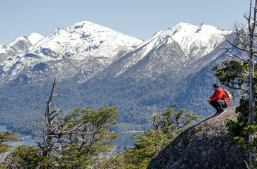 hombre en la cima de un cerro, sobre una roca, observando el paisaje de lagos y montañas nevadas