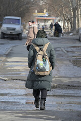 A woman with a backpack walks along the sidewalk on a spring day