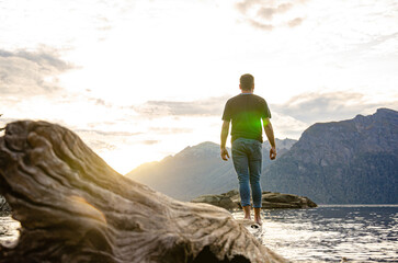 persona sobre un árbol al borde del agua de un lago en la Patagonia Argentina al atardecer con montañas de fondo mirando el paisaje