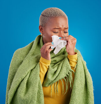 Sick black woman, tissue and blowing nose in studio, blue background or hayfever allergies, cold or winter virus. Female model, sneeze and influenza allergy of health problem, covid risk or sinusitis