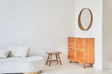 The interior of a modern living room with a round mirror on a white wall and part of a white sofa. A modern room with a chest of drawers with space for copying. High quality photo