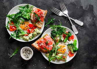 Delicious healthy breakfast - egg with vegetables, arugula salad and salmon cottage cheese toast on a dark background, top view