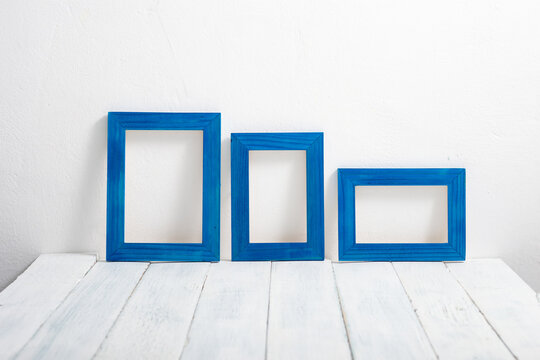 three empty blue picture frames on white wooden table