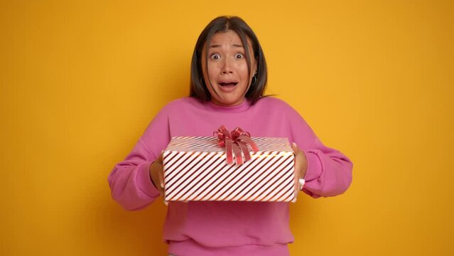 Happy Asian brunette woman get a present gift for her birthday she can't believe in that so she is amazed isolated next to yellow wall