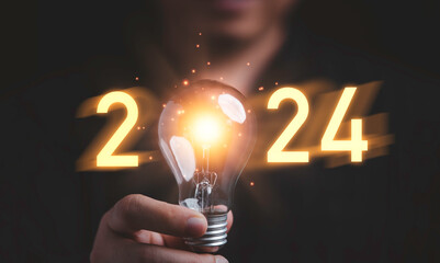 Businessman holding glowing lightbulb with 2024 number for creative thinking idea for start new...