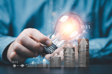 Businessman holding glowing lamp on increasing coins stacking and graph for creative thinking idea...
