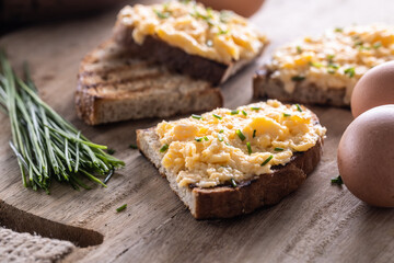Fresh scrambled eggs spread on a slice of bread with whole eggs and fresh chive on the side