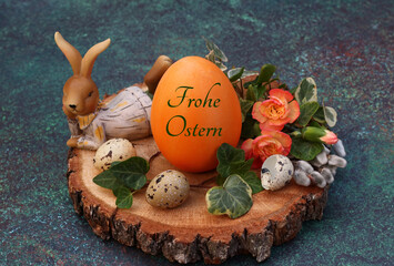Grußkarte Frohe Ostern: Beschriftetes Osterei auf einer Baumscheibe dekoriert mit Osterhasen Figur...