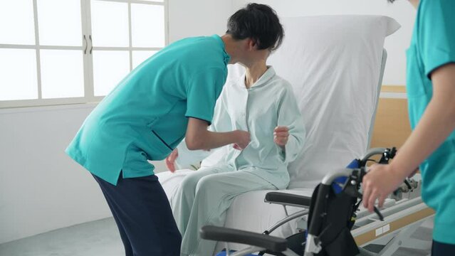高齢者を介護ベッドから車椅子に移乗させる介護士