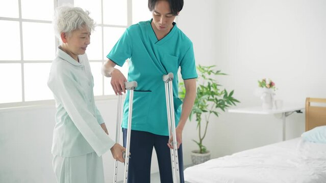 松葉杖で歩行訓練するシニア女性と介助するヘルパー