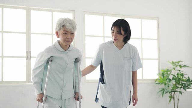 松葉杖で歩行訓練するシニア女性を介助するヘルパー