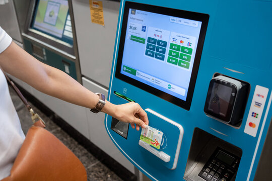 SINGAPORE - APR 19, 2022: Lady's hand placing the Singapore MRT Card (EZ-Link) at the card reader area of the ticket machine. Passenger reload EZ-Link Card using Ticket vending machine.