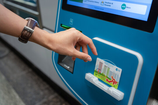 SINGAPORE - APR 19, 2022: Lady's hand placing the Singapore MRT Card (EZ-Link) at the card reader area of the ticket machine. Passenger reload EZ-Link Card using Ticket vending machine.