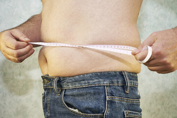 a man in jeans with a small belly measures the waist with a ribbon close-up - the concept of body positive