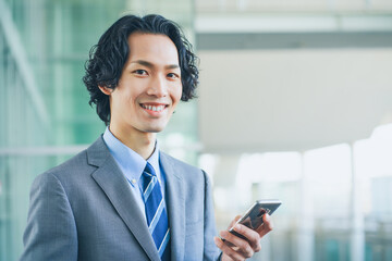 Fototapeta na wymiar オフィスの廊下でスマートフォンを操作する若いビジネスマンの男性