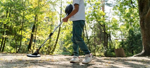 a boy with a metal detector in the park is looking for a treasure