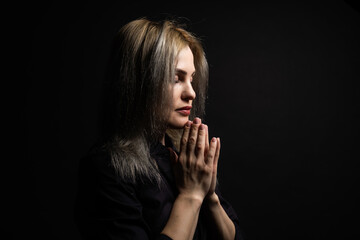 Woman praying with hands together on black background