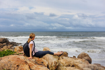 woman with backpack sitting on rock with ocean in the background