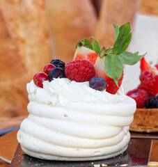 Pavlova dessert embellished with summer berries fruit, raspberries, strawberries, blueberries and currant. Closeup of the dessert at the stall at Prague farmers street food market.