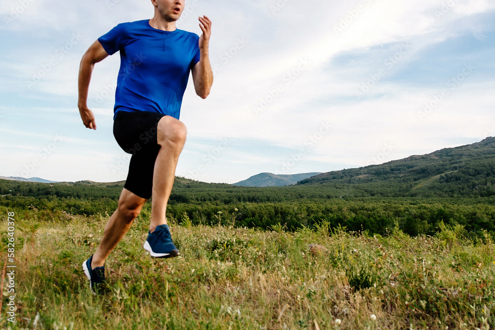 Wall mural middle age athlete runner cross-country running race, front view, blue shirt and black half tights