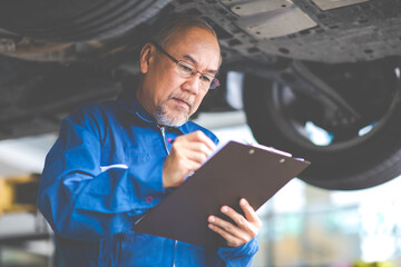 Asian Senior man mechanic working Under a Vehicle in a Car Service station. Expertise mechanic working in automobile repair garage.