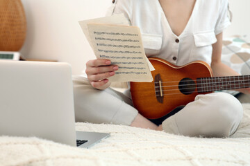 Woman learning to play ukulele with online music course at home, closeup. Time for hobby
