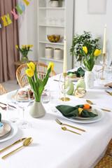 Festive Easter table setting with painted eggs, burning candles and yellow tulips in room