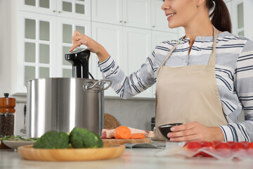 Woman using thermal immersion circulator in kitchen, closeup. Sous vide cooking
