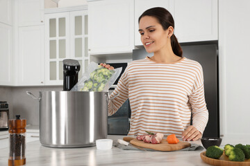 Woman putting vacuum packed broccoli into pot with sous vide cooker in kitchen. Thermal immersion...