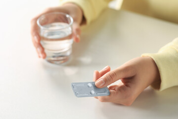 Woman taking emergency contraception pill at white table indoors, closeup