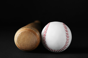 Wooden baseball bat and ball on black background, closeup. Sports equipment