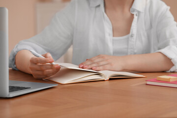 Woman with notebook at wooden table indoors, closeup