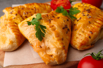 Fresh delicious puff pastry with cheese, tomatoes and parsley on wooden board, closeup