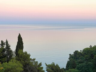 Naklejka premium Sunrise sky over calm sea water and coastal forest.