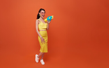 cheerful tourist woman traveling with water gun during Songkran festival studio on copy space orange background.