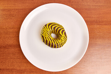 Donut with sweet filling covered with chocolate on a white plate. The concept of baking delicious donuts.