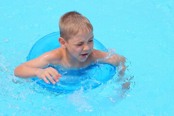 Fototapeta na wymiar Funny little boy swims in a pool in an blue ring top view