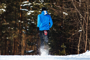 back male runner running winter trail, splashes of snow underfoot, sports photo