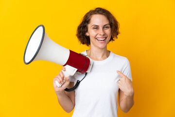 Young English woman isolated on yellow background holding a megaphone and with surprise facial...