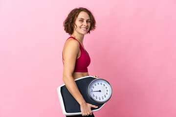 Young English woman isolated on pink background with weighing machine
