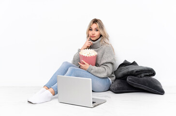 Teenager blonde girl eating popcorn while watching a movie on the laptop and looking front