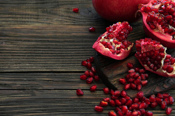 Juicy, ripe, red pomegranate on a wooden old table, beautifully decorated and close-up shot. Pomegranate pieces are surrounded by pomegranate seeds.