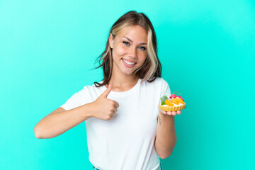 Young Russian woman holding a fruit sweet isolated on blue background giving a thumbs up gesture