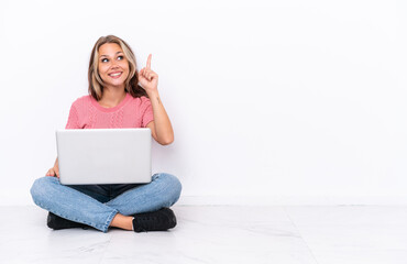Young Russian girl with a laptop sitting on the floor isolated on white background intending to realizes the solution while lifting a finger up