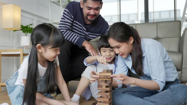 Family relaxing on sofa while kid drawing on floor. Happy Asian little girl enjoy playing a stacking blocks with her parent in living room in free time.